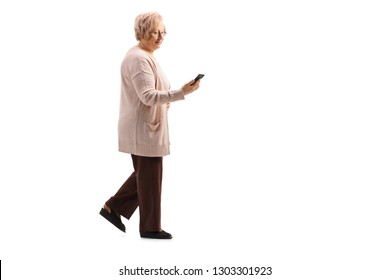 Full Length Profile Shot Of An Older Lady Walking And Using A Cell Phone Isolated On White Background