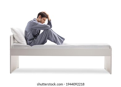 Full Length Profile Shot Of A Sad Man In Pajamas Sitting On A Single Bed Isolated On White Background