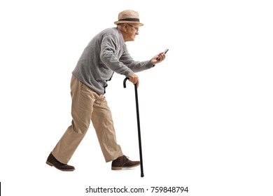 Full Length Profile Shot Of A Senior With A Cane Walking And Looking At A Phone Isolated On White Background