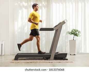 Full length profile shot of a smiling young man running on a treadmill at home - Powered by Shutterstock