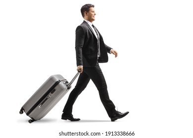 Full length profile shot of a smiling young businessman walking and pulling a suitcase isolated on white background