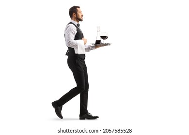 Full length profile shot of a waiter carrying a red wine decanter on a silver tray and walking isolated on white background