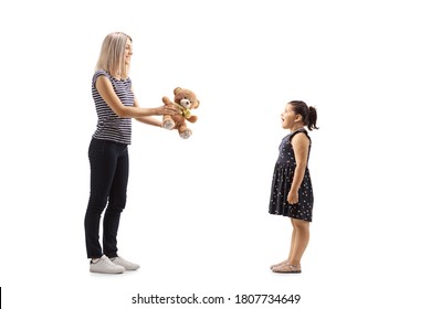 Full Length Profile Shot Of A Woman Giving A Teddy Bear To A Girl  Isolated On White Background