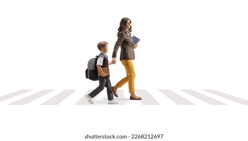 Full length profile shot of a woman carrying books and holding hands with a schoolboy on a pedestrian crossing isolated on white background