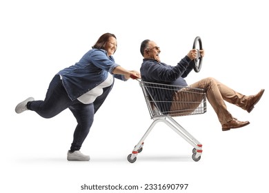 Full length profile shot of a woman pushing a mature man with a steering wheel inside a shopping cart isolated on white background
