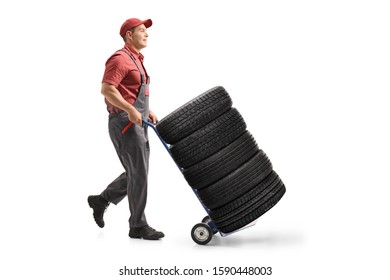 Full length profile shot of a worker pushing car tires with a hand truck isolated on white background