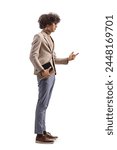 Full length profile shot of a young man holding a book and talking isolated on white background