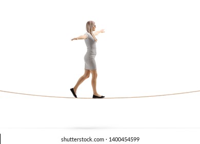 Full length profile shot of a young blond woman walking on a rope with arms spread isolated on white background