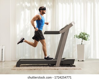 Full length profile shot of a young man running on a treadmill and wearing a vr headset at home 