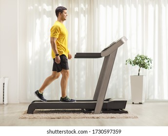 Full Length Profile Shot Of A Young Man Walking On A Treadmill At Home