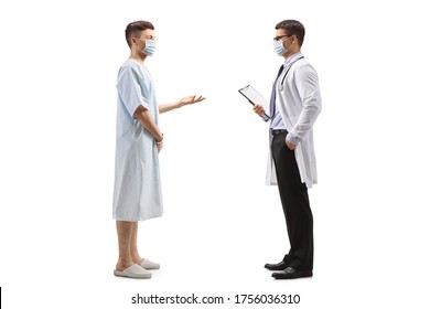 Full Length Profile Shot Of A Young Male Patient In A Hospital Gown Talking To A Doctor And Wearing Protective Masks Isolated On White Background