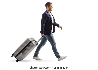 Full length profile shot of a young man smiling and walking with a suitcase isolated on white background
