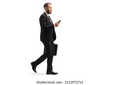 Full length profile shot of a young businessman walking and using a mobile phone with a briefcase in his hands isolated on white background