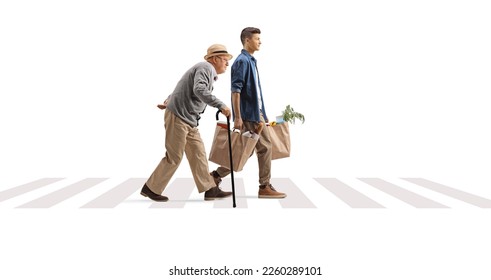 Full length profile shot of a young man helping a senior with grocery bags on a pedestrian crossing isolated on white background