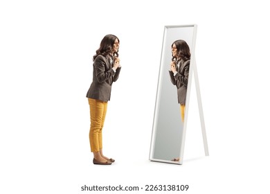 Full length profile shot of a young woman getting ready in front of a mirror and putting a scarf isolated on white background