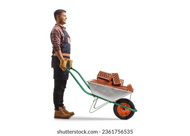 Full length profile shot of a young man standing with a wheelbarrow full of bricks isolated on white background