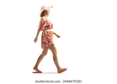 Full length profile shot of a young woman in a summer dress and straw hat walking isolated on white background