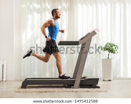 Full length profile shot of a young man running on a treadmill at home 