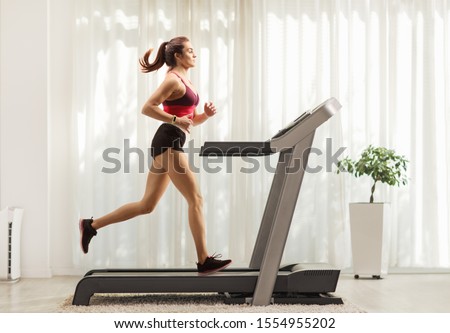 Full length profile shot of a young woman running on a treadmill at home