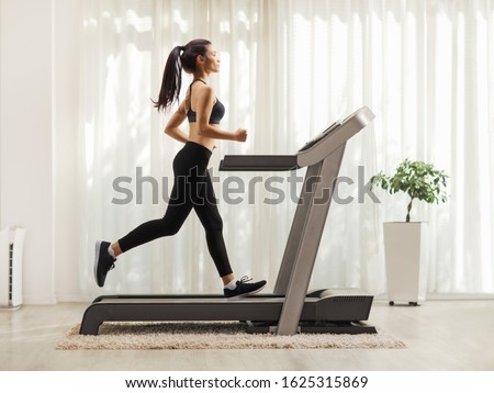 Full length profile shot of a young woman running on a treadmill indoors