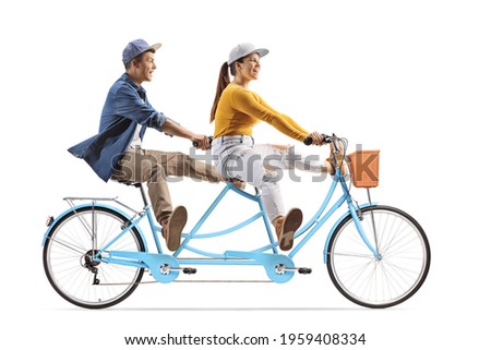 Full length profile shot of a young male and female riding a tandem bicycle and lifitng legs isolated on white background