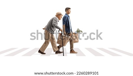 Full length profile shot of a young man helping a senior with grocery bags on a pedestrian crossing isolated on white background