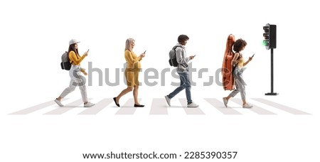 Full length profile shot of young people crossing street at a pedestrian crossing and using mobile phones isolated on white background