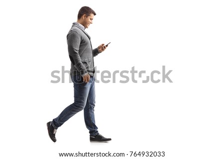 Full length profile shot of a young man walking and using a phone isolated on white background