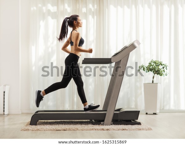 Full length profile shot of a young woman running on a treadmill indoors