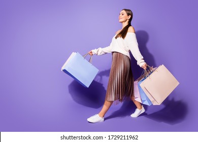 Full length profile side photo of positive satisfied girl enjoy shopping go walk copyspace store mall hold many bags wear brown sweater footwear isolated purple color background