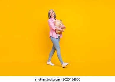 Full length profile side photo of aged woman happy positive smile go hold shopping bag food isolated over yellow color background - Powered by Shutterstock