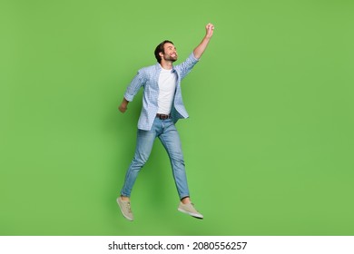 Full length profile side photo of young guy try to catch parasol look empty space jump isolated over green color background