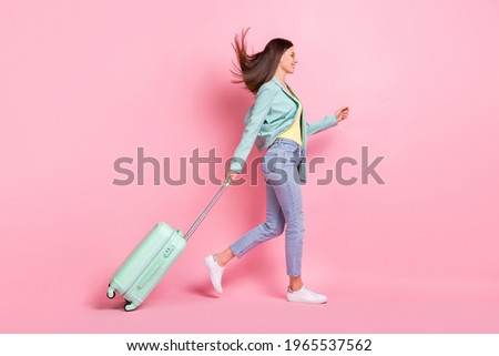Full length profile side photo of charming pretty young lady walk empty space travel bag isolated on pink color background