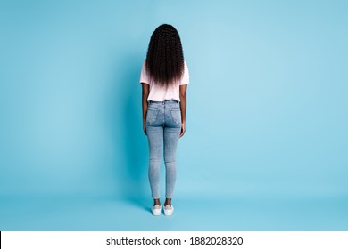 Full Length Rear Behind View Photo Of Pretty Slim Afro Woman Wear Pink T-shirt Jeans Hands Arms Down Isolated Blue Color Background