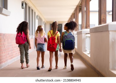 Full length rear view of multiracial elementary schoolgirls with backpacks walking in corridor. unaltered, childhood, together, education and back to school concept.