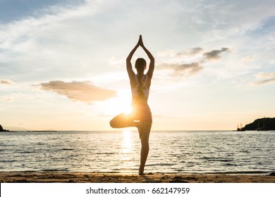Full length rear view of the silhouette of a woman standing on one leg while practicing the tree yoga pose on a tranquil beach, shot at sunset during summer vacation in Indonesia