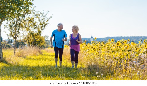 Full length rear view of two healthy senior people jogging on a country road against clear blue sky in summer