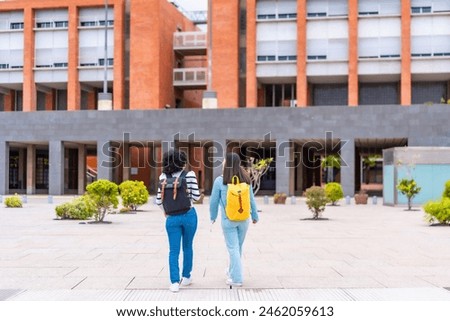 Full length rear view of two multi-ethnic women walking outside the university to the entrance