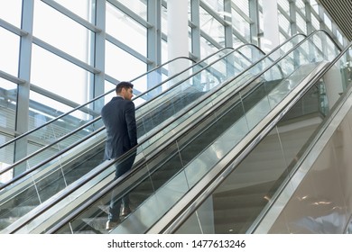 Full length rear view of young Caucasian businessman going up an escalator in a modern office building. Modern corporate start up new business concept with entrepreneur working hard - Powered by Shutterstock