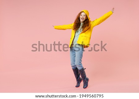 Full length redhead young woman in yellow waterproof raincoat outerwear stand on toes dancing leaning back isolated on pastel pink background studio Outdoors lifestyle wet fall weather season concept