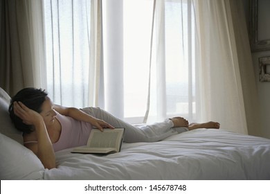 Full length of relaxed woman reading book in bed