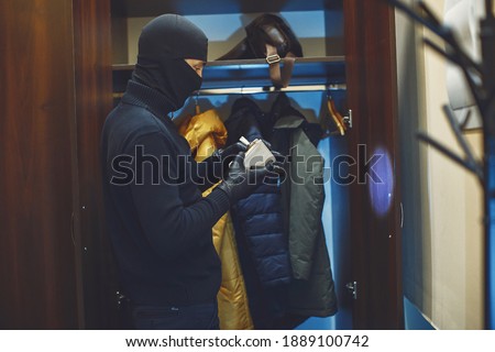 Full length of robber. Man with flashlight and bag in living room. Robber pulls things out of the closet.