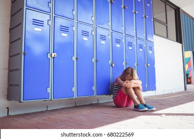 Full length of schoolgirl sitting on pavement by lockers in corridor at school - Powered by Shutterstock