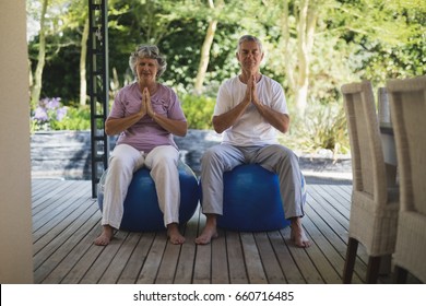 Full length of senior couple meditating together while sitting on exercise balls at porch - Powered by Shutterstock