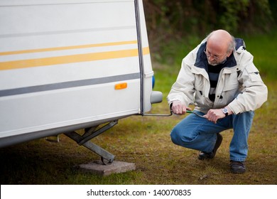 Full Length Of Senior Man Crouching While Repairing Caravan In Forest