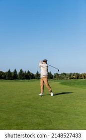 Full Length Of Senior Man In Flat Cap Playing Golf On Green Lawn