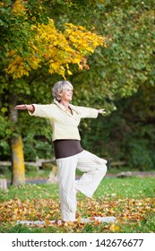 Full Length Of Senior Woman With Arms Outstretched Standing On One Leg While Doing Yoga In Park