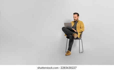 Full length of serious focused mid adult male professional dressed in casual working over laptop while sitting on chair against white background - Powered by Shutterstock