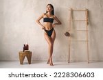 Full length shot of asian woman posing in black bikini near wall in the bathroom