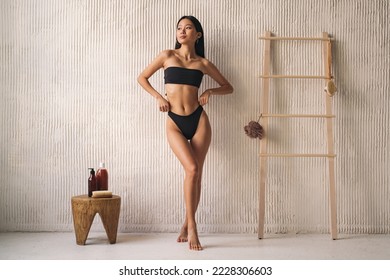 Full length shot of asian woman posing in black bikini near wall in the bathroom